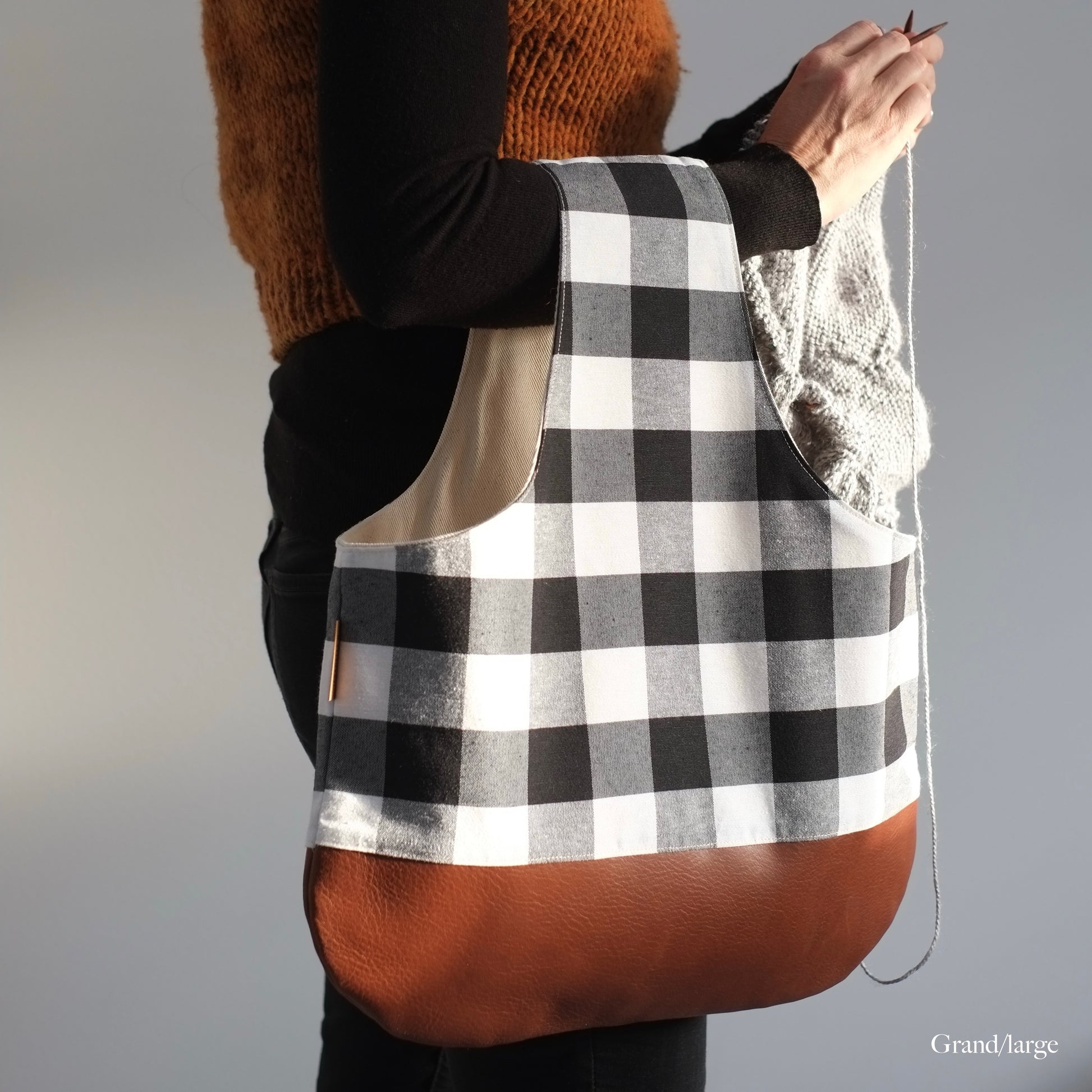 Lady standing and knitting with a large black and whit bag that has a brown leather bottom