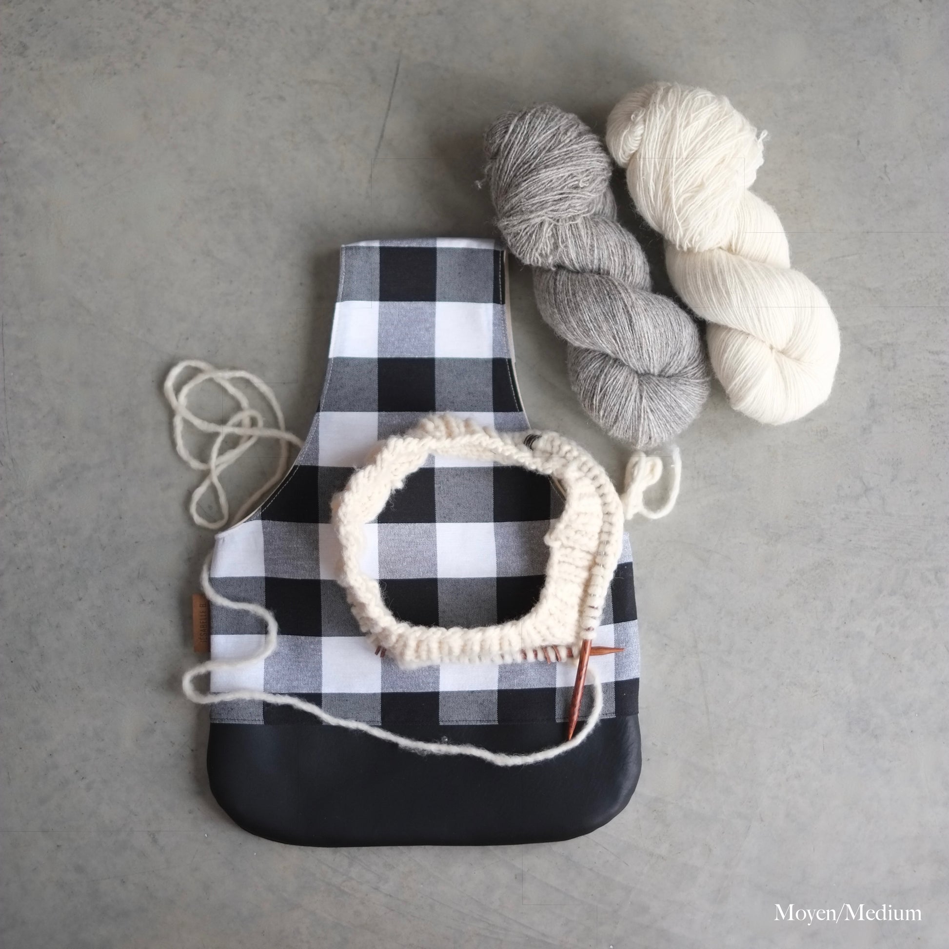 Top view of a black and white buffalo plaid knitting bag with a black leather bottom and yarn