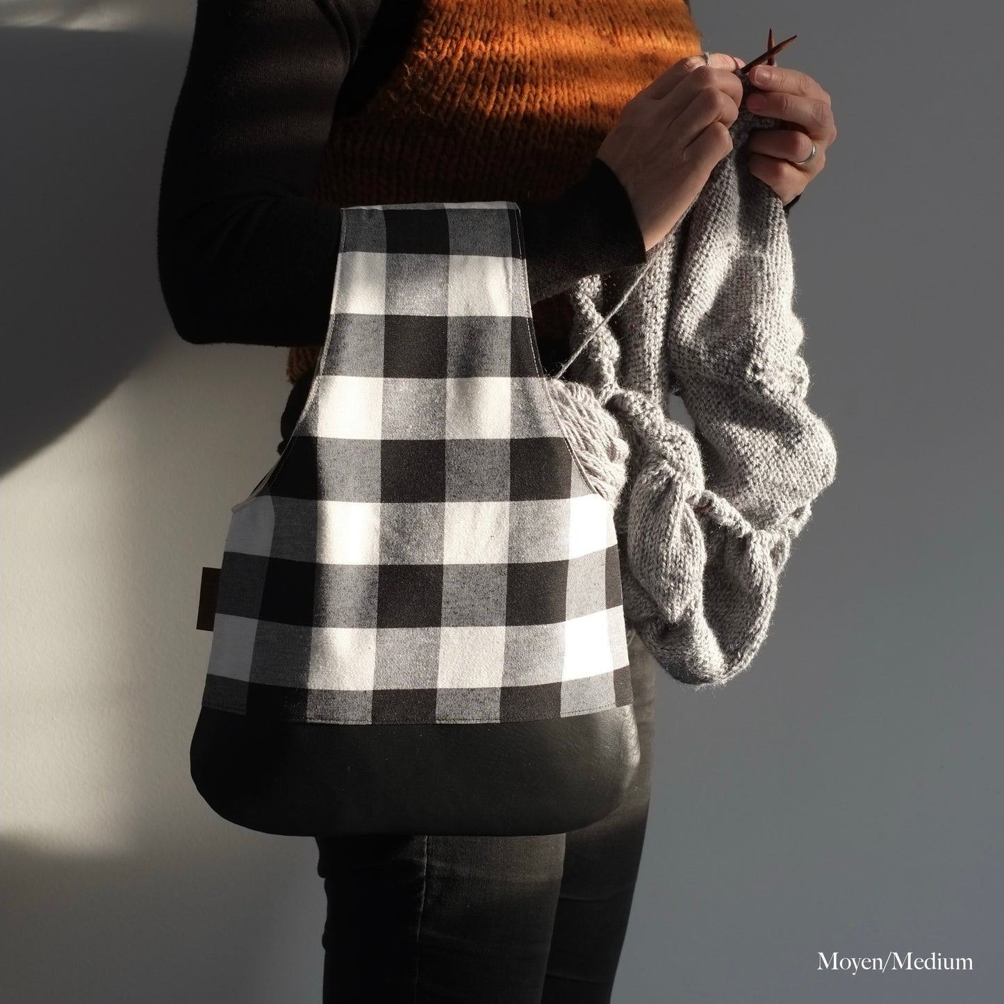 Woman standing and knitting with a project wristlet in black and white with a black leather bottom