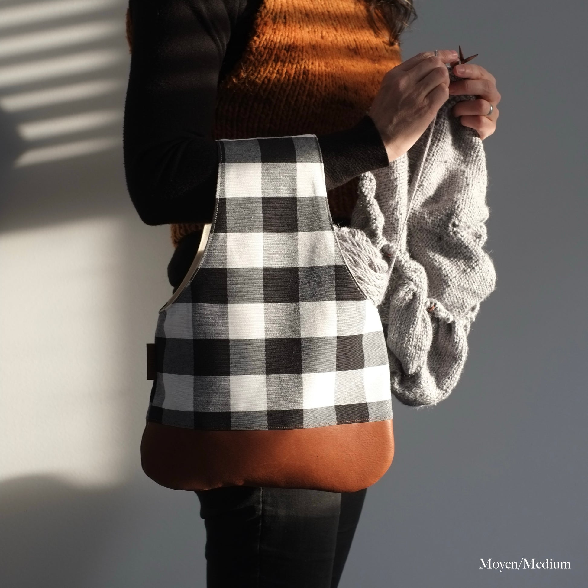Woman knitting with a medium black and white arm bag that has a brown leather bottom