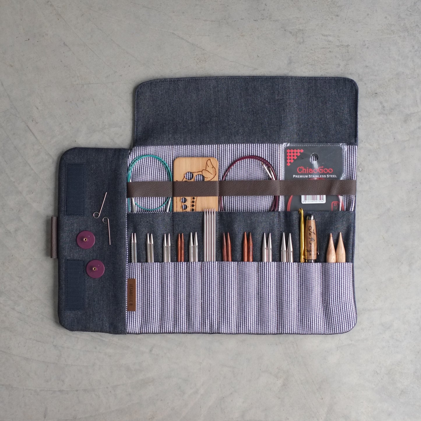 Vue de haut de l'étui d'aiguilles denim bleu foncé ouvert — aiguilles, pointes, doubles pointes, crochets, câbles et jauge de mesure parfaitement rangés, Jésabelle B. | Top view of dark denim needle organizer open — needles, tips, DPNs, hooks, cables and gauge neatly organized, Jésabelle B.
