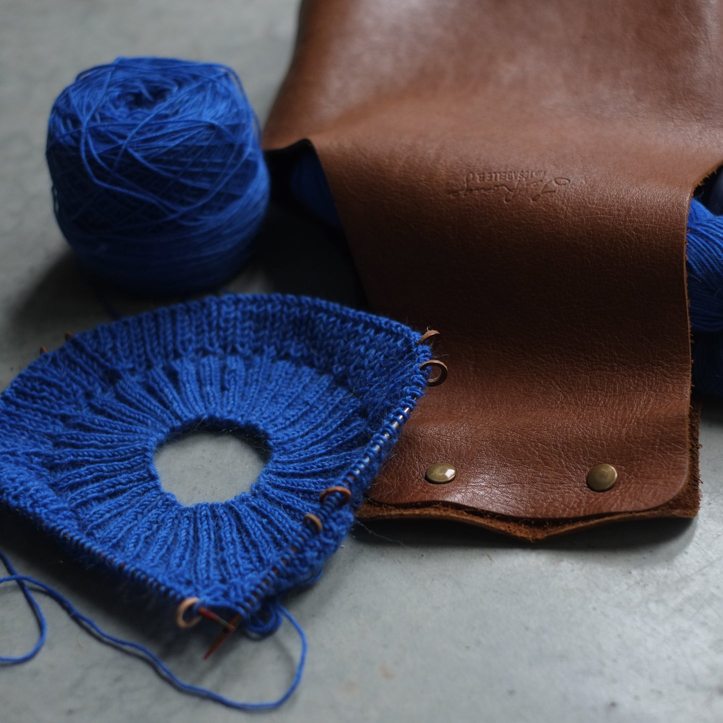 Close-up of a brown leather bag and the embossed signature and the snaps to close / Gros plan sur un sac de tricot de cuir avec la signature embossée et la fermeture avec boutons pression