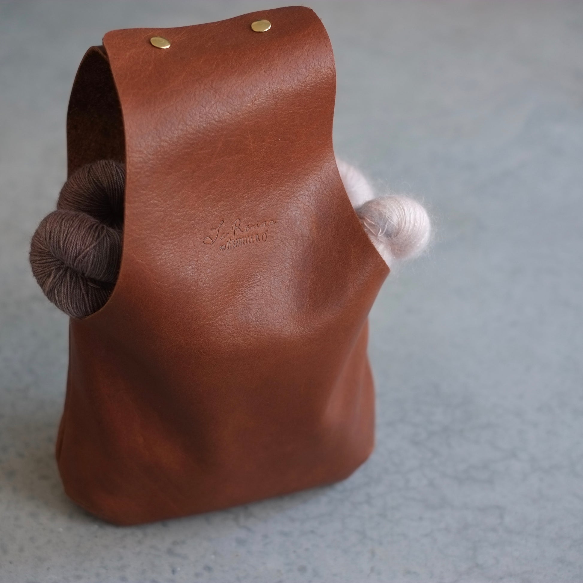 Complete vue of a brown leather knitting bag with some soft yarn inside / Vue complète du sac de cuir brun à tricot ou crochet avec de la laine douce à l'intérieur