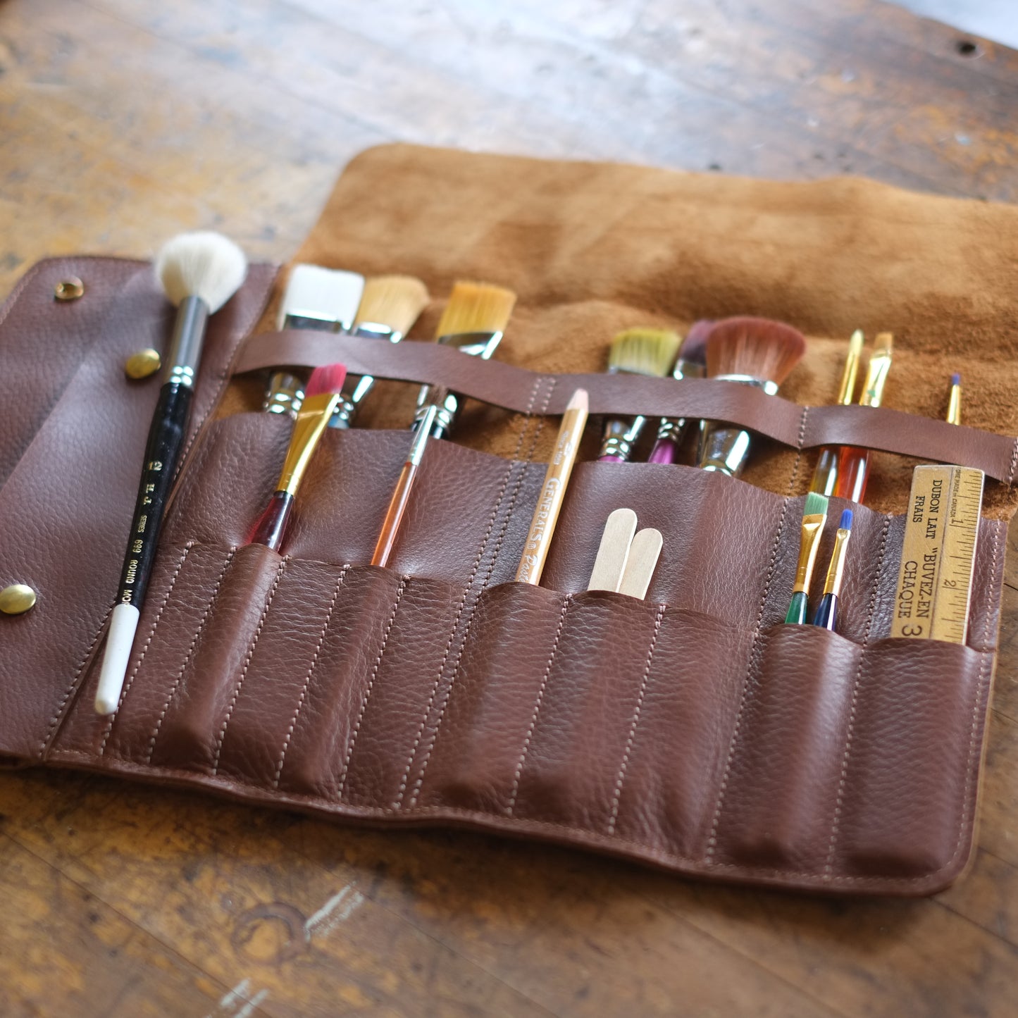 Open brown leather needle case on wood table — versatile storage for creative tools / Étui en cuir brun ouvert sur table en bois — rangement polyvalent pour outils créatifs