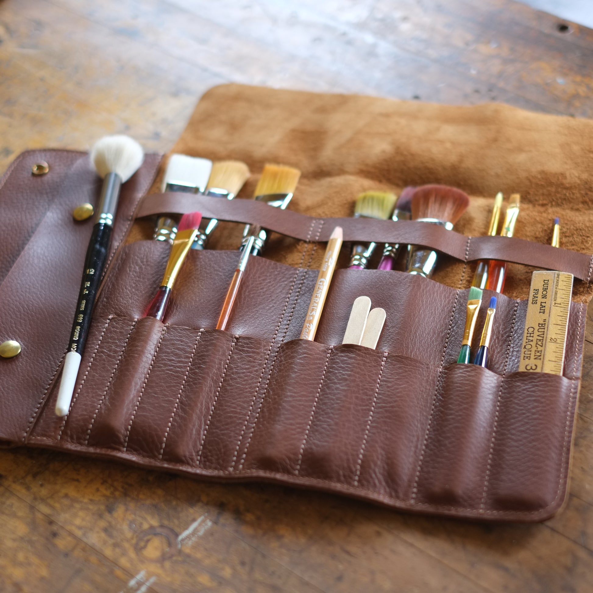 Open brown leather needle case on wood table — versatile storage for creative tools / Étui en cuir brun ouvert sur table en bois — rangement polyvalent pour outils créatifs