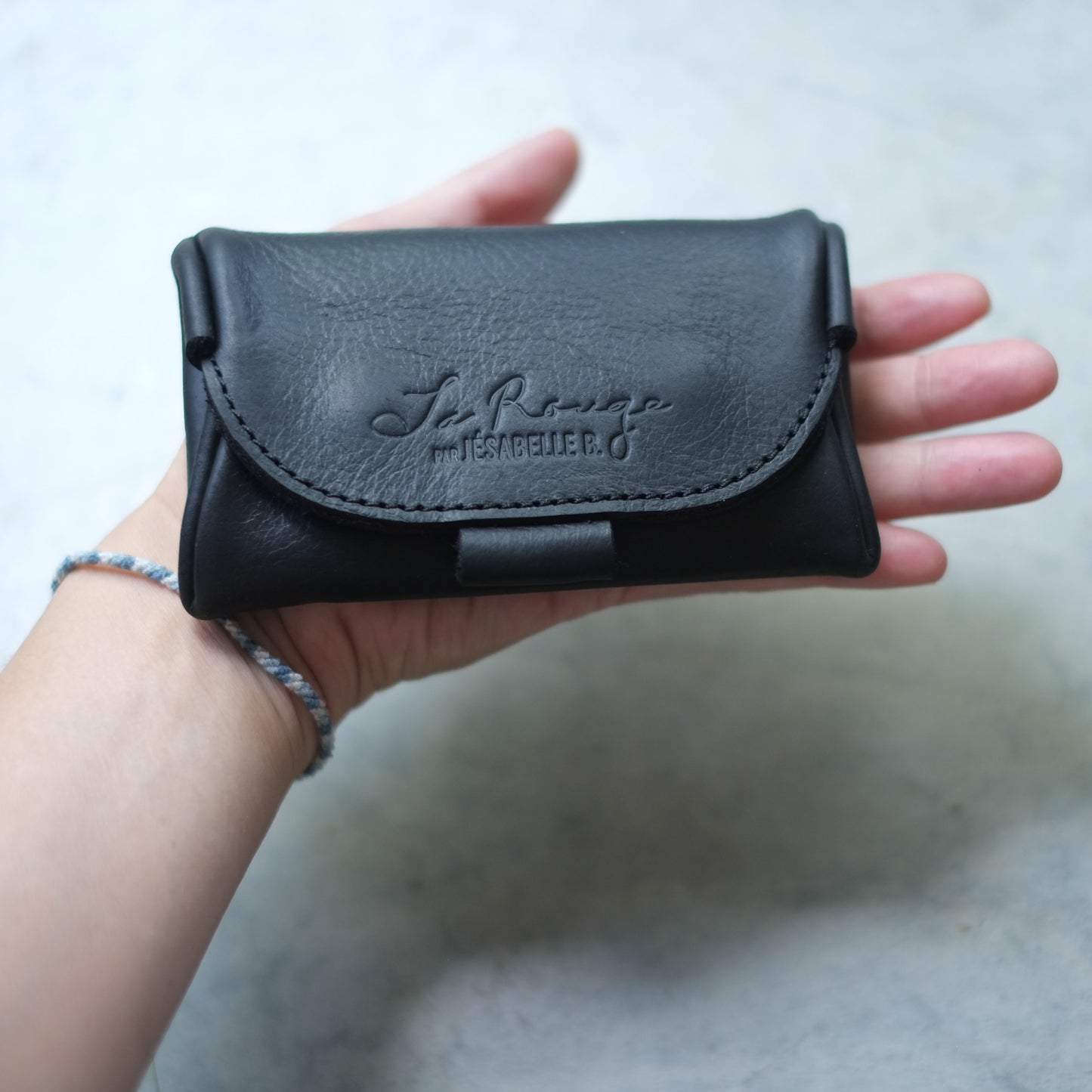 Main tenant l'étui mini de cuir noir La Rouge, embossage visible | Hand holding La Rouge black leather mini case, embossing visible
