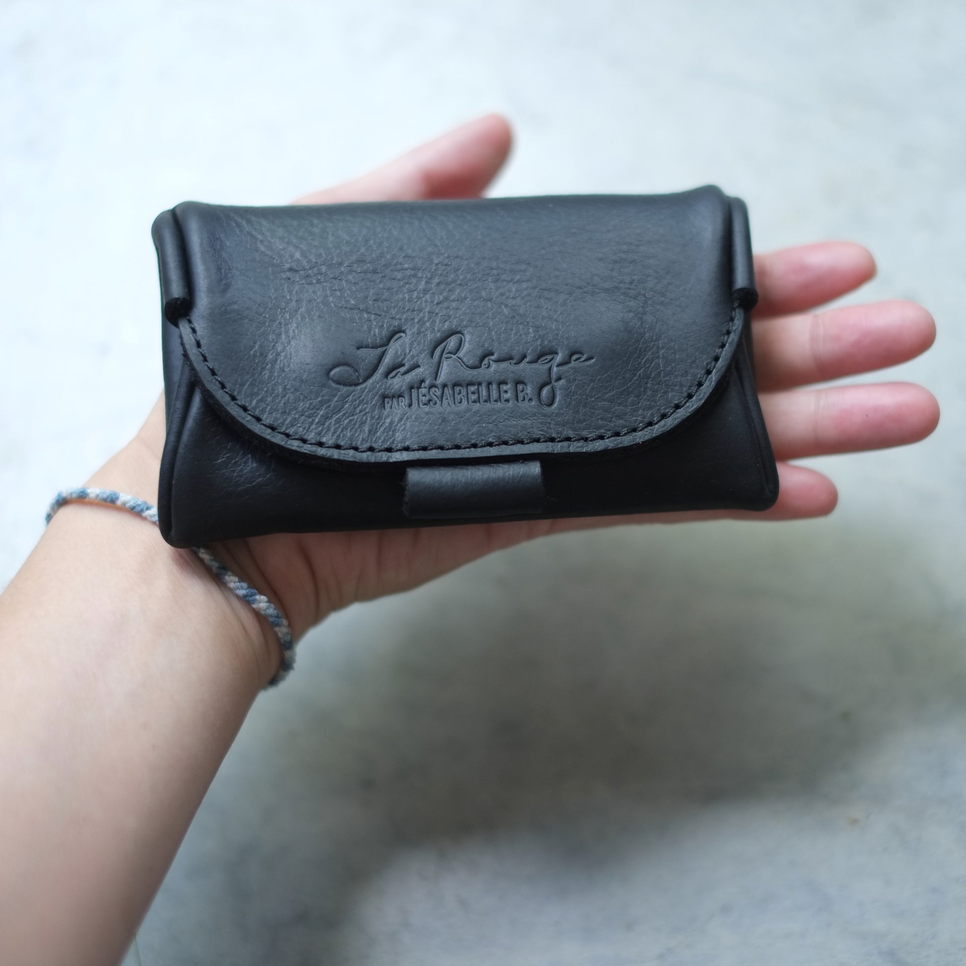 Main tenant l'étui mini de cuir noir La Rouge, embossage visible | Hand holding La Rouge black leather mini case, embossing visible

