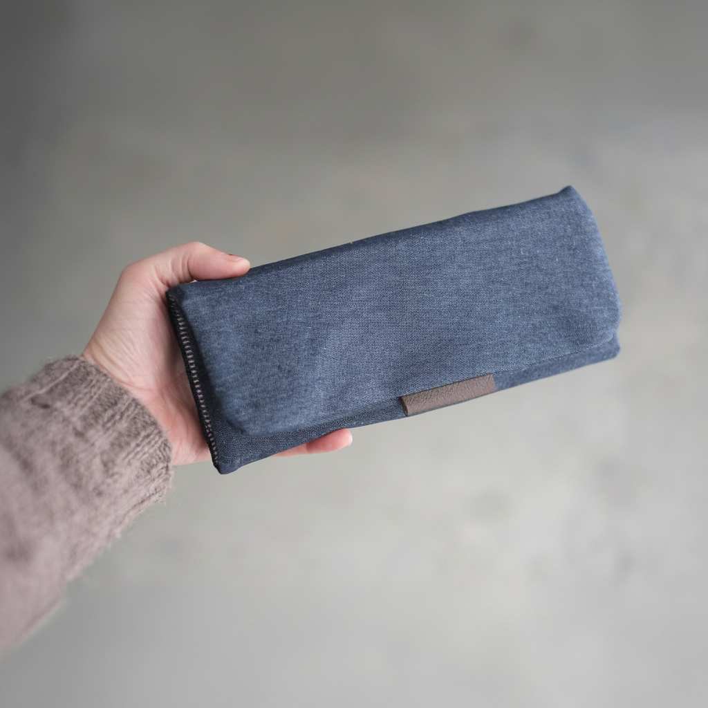 Étui d'aiguilles en denim bleu foncé fermé tenu à la main — format plat et compact, idéal cadeau tricoteuse, fait main au Canada, Jésabelle B. | Dark denim knitting needle case closed held in hand — flat and compact, perfect gift for knitters, handmade in Canada, Jésabelle B.