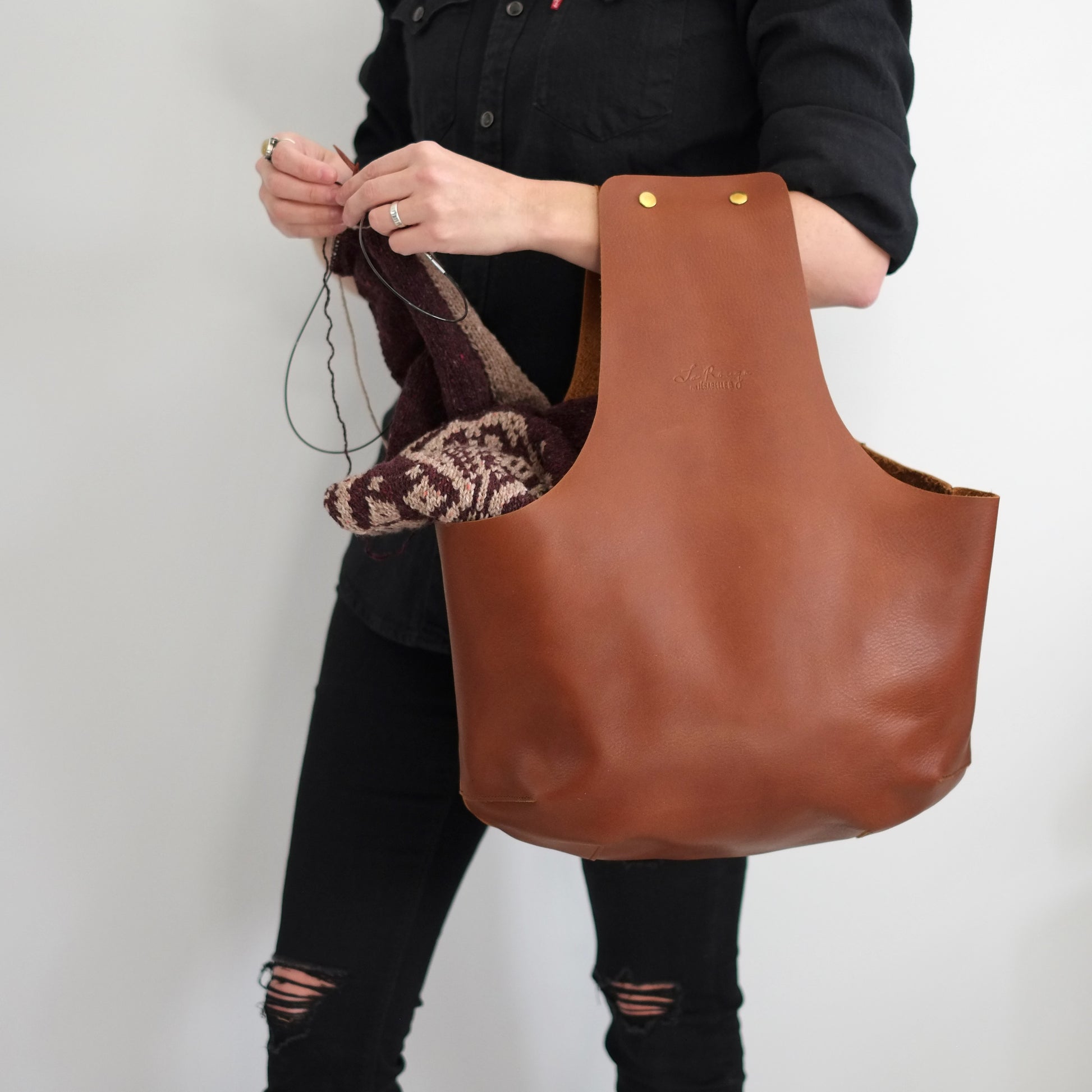 Une tricoteuse utilisant le sac de tricot ultime en cuir brun pour tricoter son chandail avec les mains libres