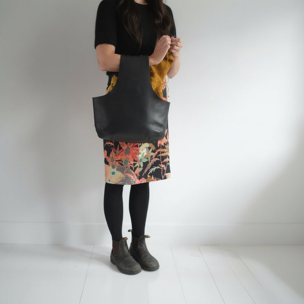 Knitter standing and using a lack leather arm bag to knit hands-free / Une tricoteuse debout qui utilise un sac de cuir noir au bras pour tricoter les mains libres