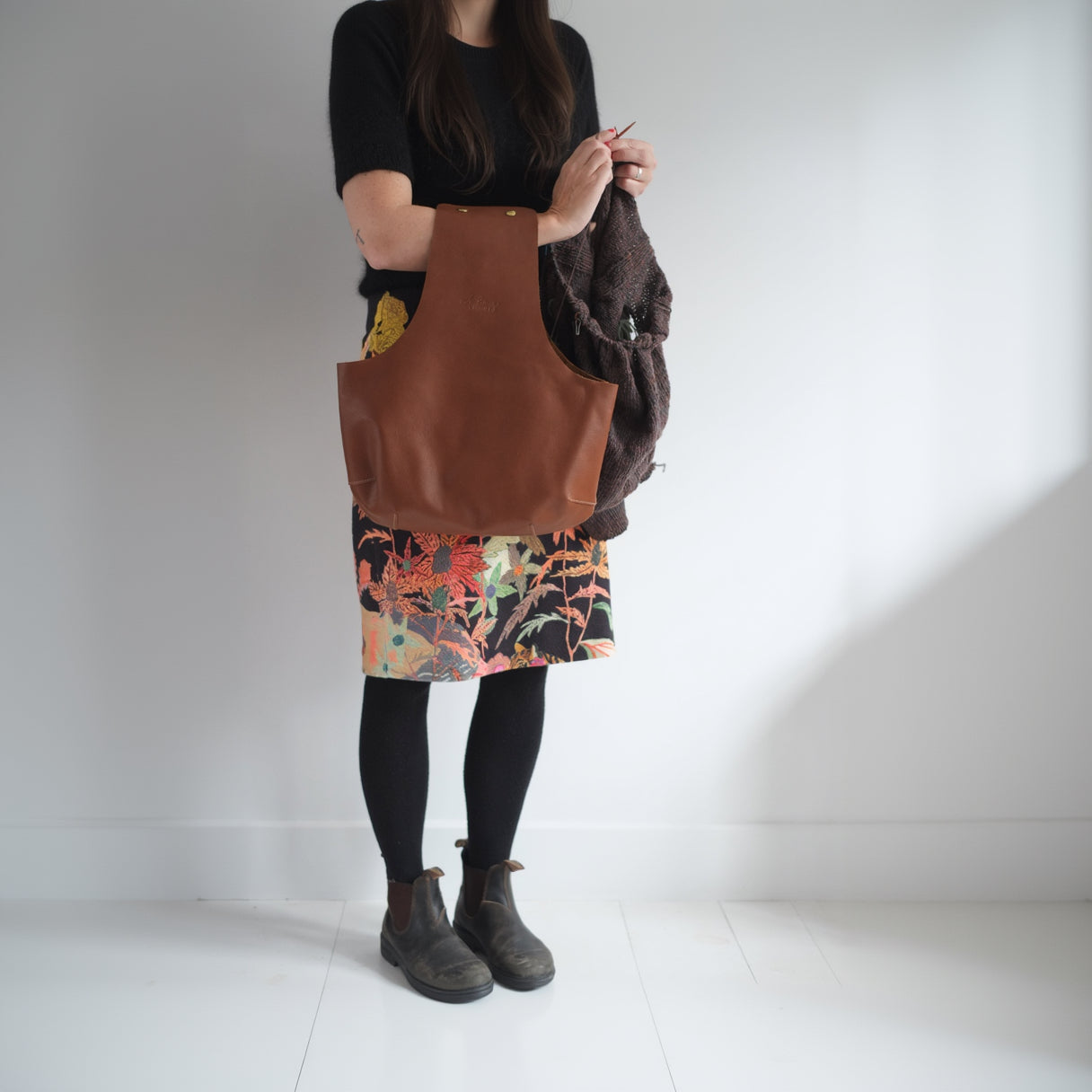 Knitter standing and using a brown leather arm bag to knit hands-free / Une tricoteuse debout qui utilise un sac de cuir brun au bras pour tricoter les mains libres