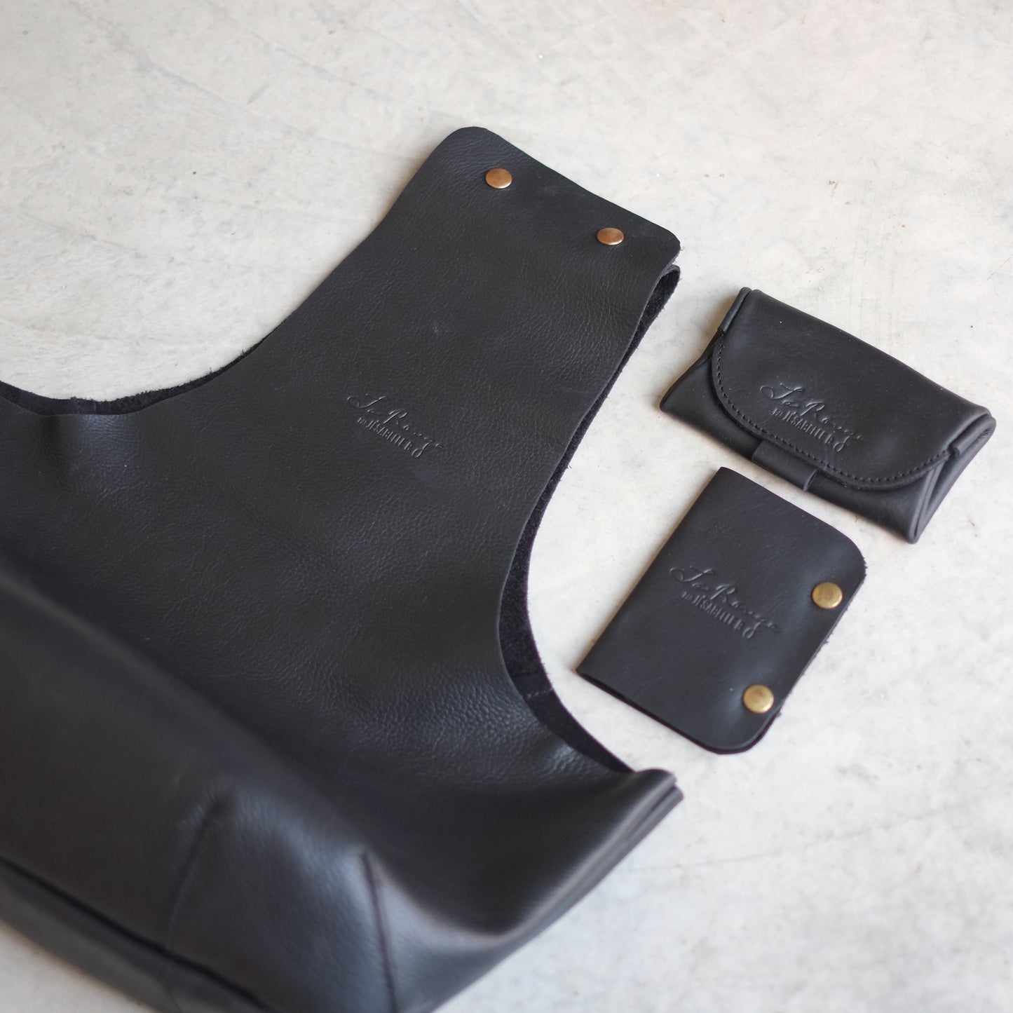 In-Between sized black leather bag embossed with La Rouge signature with matching case and booklet / Le sac de tricot en cuir noir La Rouge embossé de sa signature au côté d'un mini étui et d'un livret de cuir coordonnés