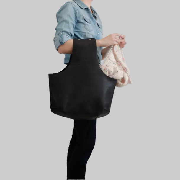 Large project bag in black leather worn on wrist by knitter knitting away / Grand sac de projet tenu sur le bras par une tricoteuse tricotant