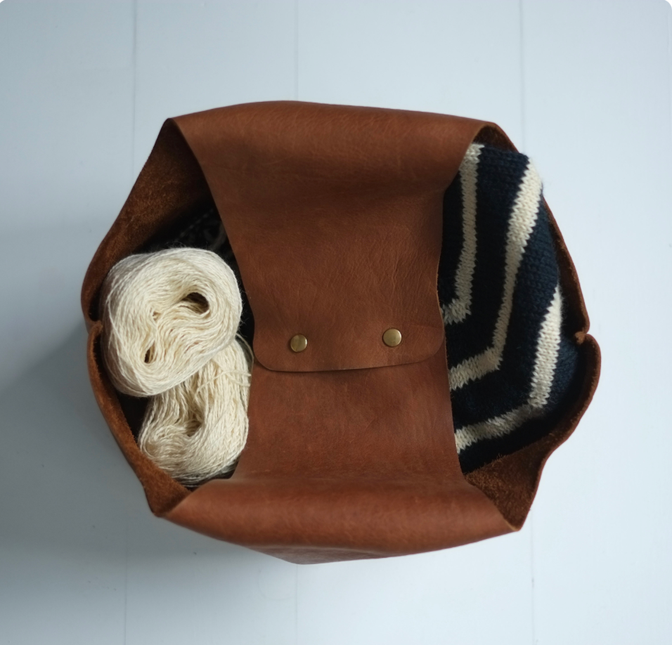 Top view of the closed leather knitting bag containing a whole knitted sweater and yarn / Vue de haut du sac de cuir fermé avec un chandail complet et de la laine dedans