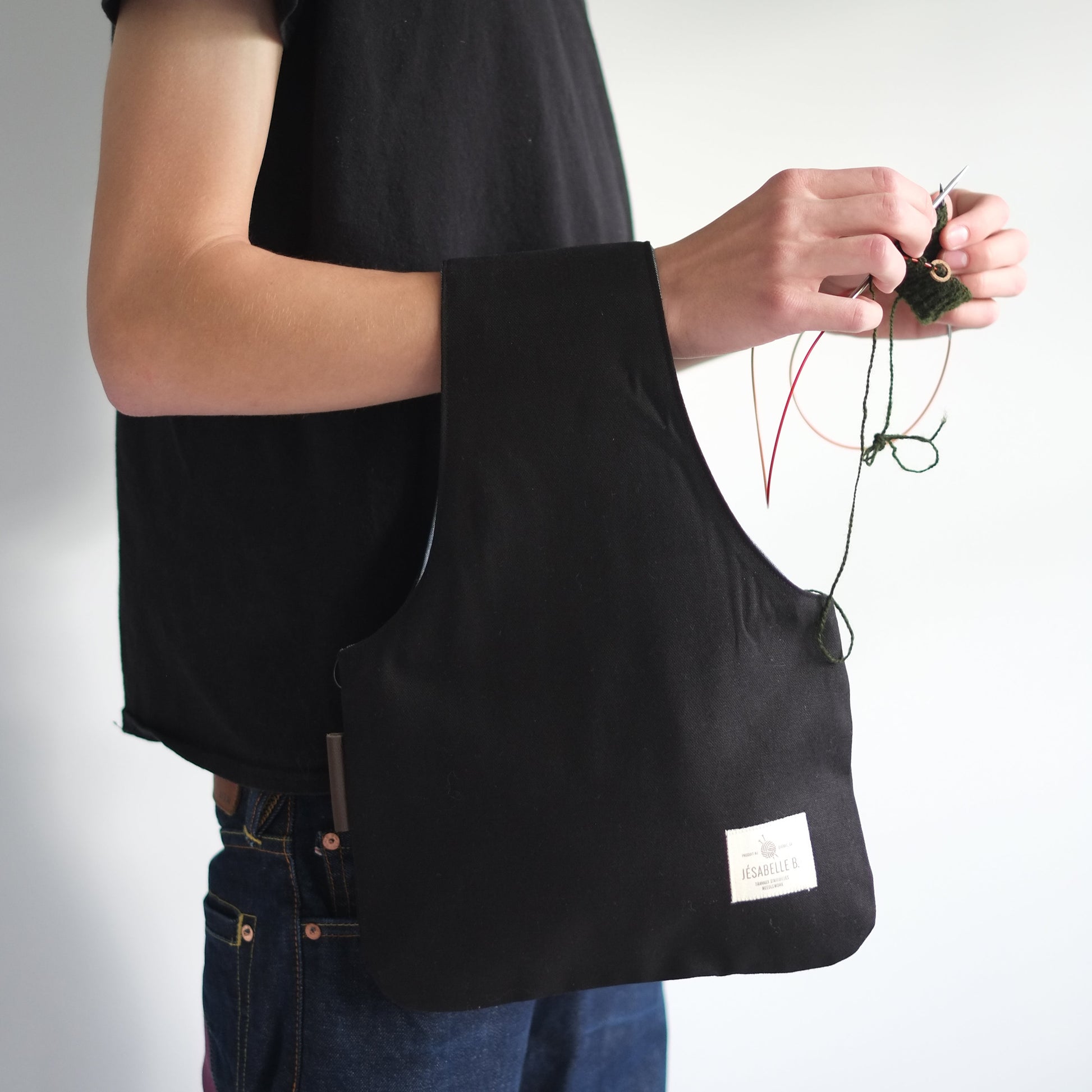 Man knitting hands-free with medium black canvas knitting bag on wrist — original gift for knitters / Sac de tricot en canevas noir au poignet d'un homme qui tricote les mains libres