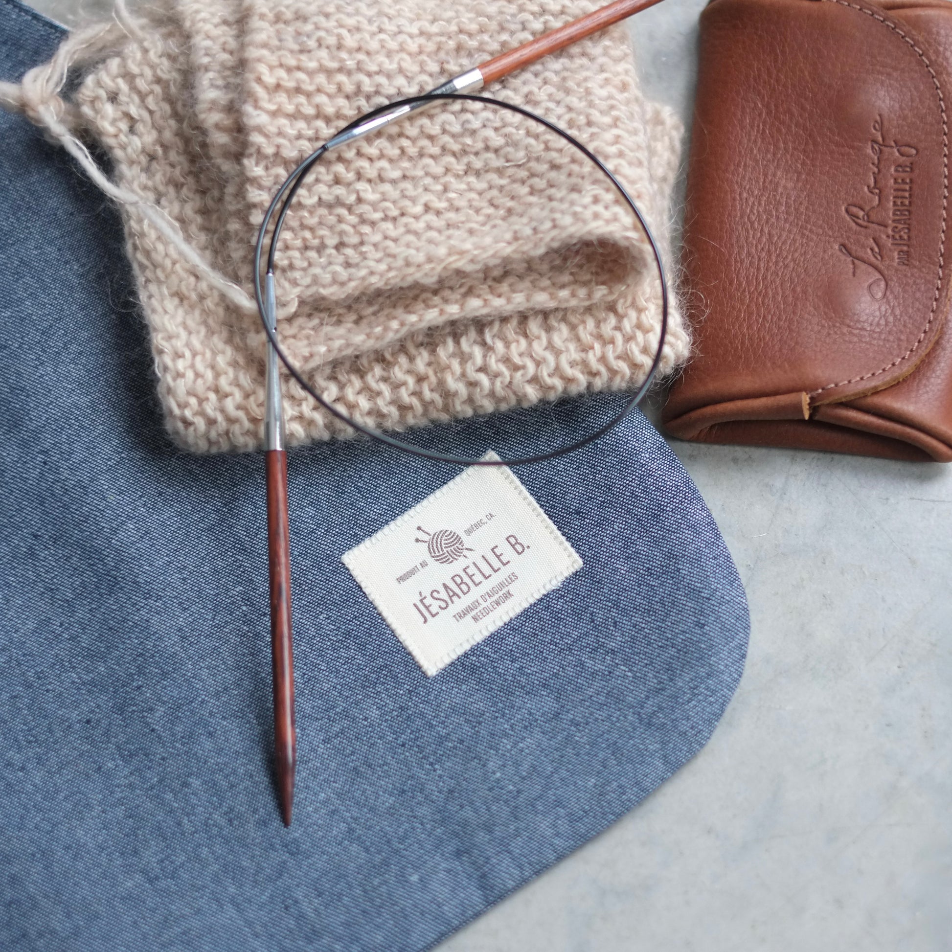 Close-up of grey-blue denim fabric and Jésabelle B. label with knitting and brown leather case / Gros plan sur le denim gris-bleu et l'étiquette Jésabelle B. avec tricot et petit étui de cuir brun