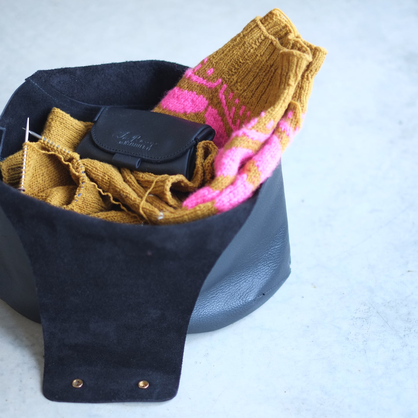 An open leather bag with a sweater project ready to knit / Un sac de tricot en cuir noir ouvert montrâtes un projet chandail en cours de tricot