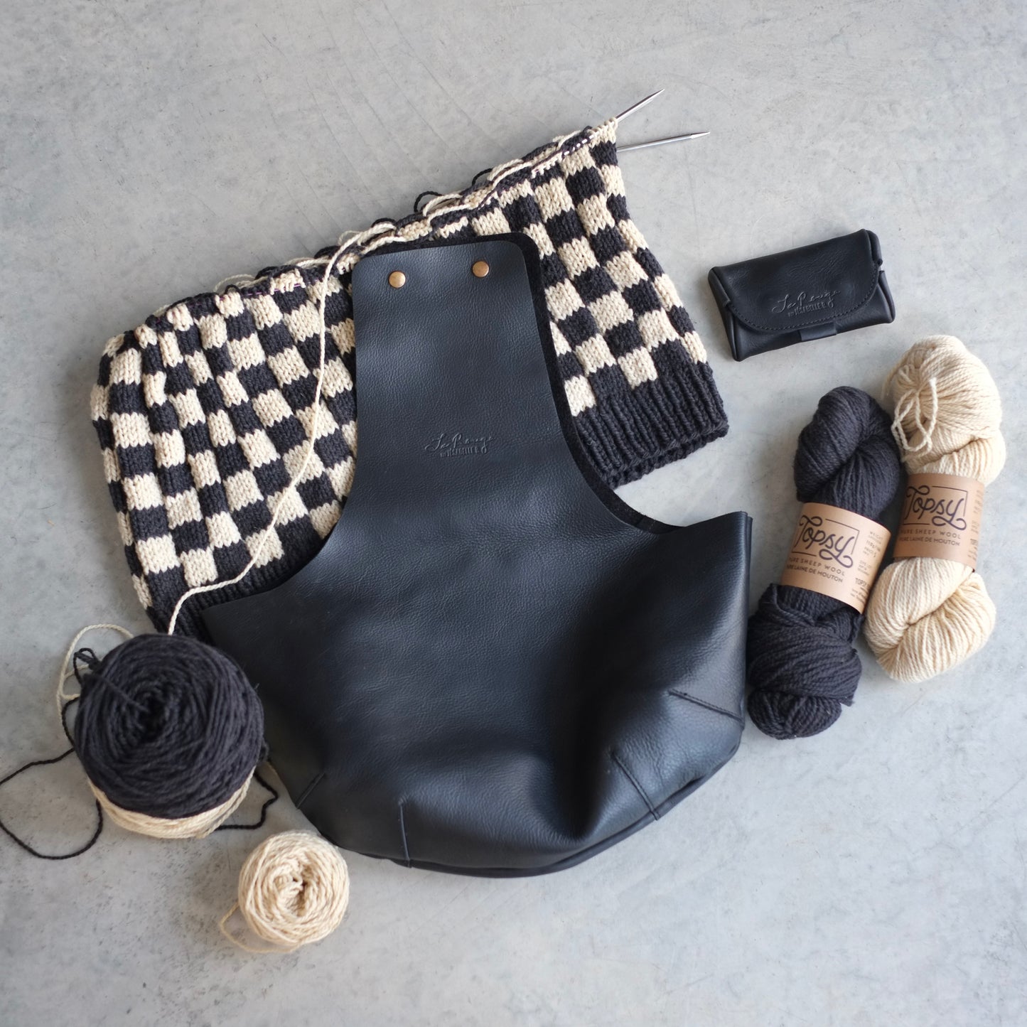 The in-between bag is the perfect size for a sweater project, view from top with embossed signature on leather / Vue de haut avec la signature embossée sur le cuir noir du sac entre-deux pour le tricot d'un chandail