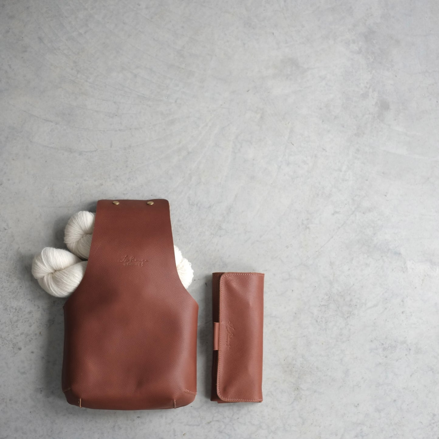 Top vue of the medium brown leather knitting bag with 2 yarn skein inside and a matching leather case beside / Vu de haut du sac de tricot moyen avec 2 écheveaux de laine à l'intérieur et un étui d'aiguilles à côté