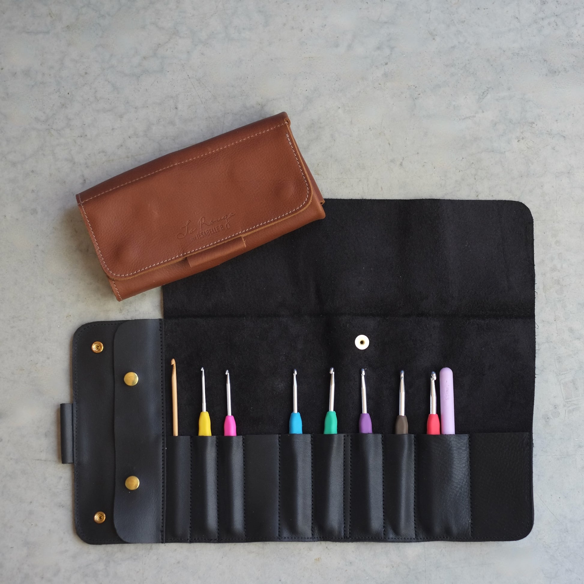 tui en cuir noir pour crochets ouvert — rabat de protection, poche latérale, 10 espaces, étui brun fermé en arrière-plan, Jésabelle B. | Black leather crochet hook case open — protective flap, side pocket, 10 slots, brown case closed in background, Jésabelle B.
